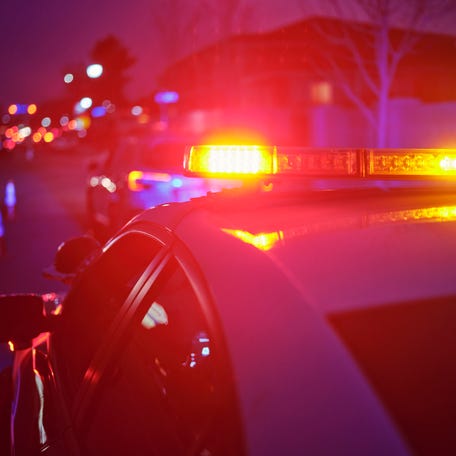 A police car at night alongside a road with emergency lights flashing.