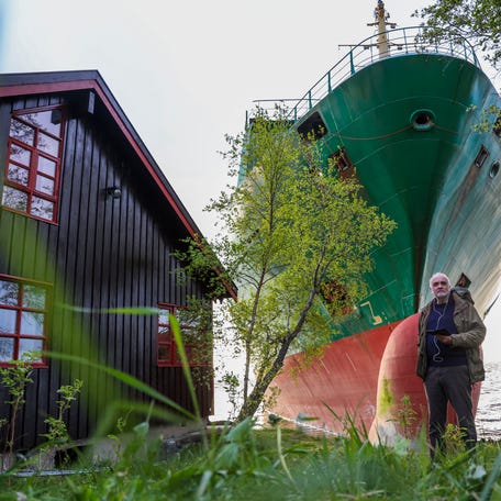 Johan Helberg's pose next to his house and a 135-meter-long container ship by the shore in the Trondheimsfjord outside Byneset by Trondheim, Norway, on May 22, 2025, after the ship ran aground almost hitting his house.