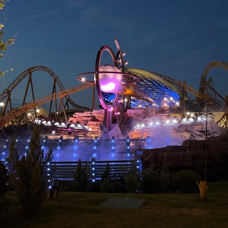 Stardust Racer's illuminated cars zip along unlit track in Universal Epic Universe's Celestial Park at night.