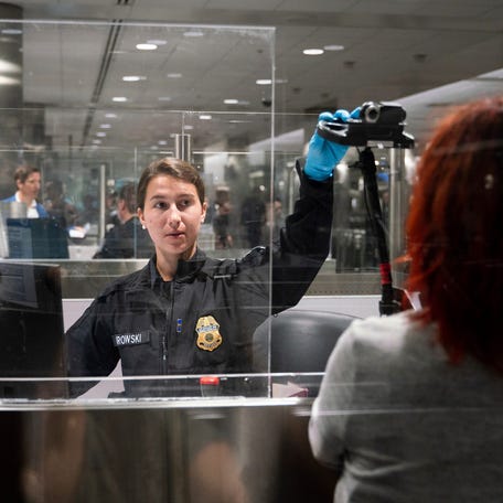 CBP officer G. Barowski, center, uses a camera with facial recognition biometrics to verify international travelers Henning Radtke, left, and Jeanette Radtke upon entering U.S. Customs and Border Protection at McNamara Terminal at Detroit Metro Airport in Romulus on Friday, July 28, 2023.
