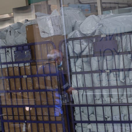 Parcels waiting to be processed are seen through a glass as a delivery worker's reflection appears on it in a post office, as Hong Kong Post stops certain U.S.-bound shipments since April 27 due to new U.S. tariff rules, in Hong Kong, China, May 2, 2025.