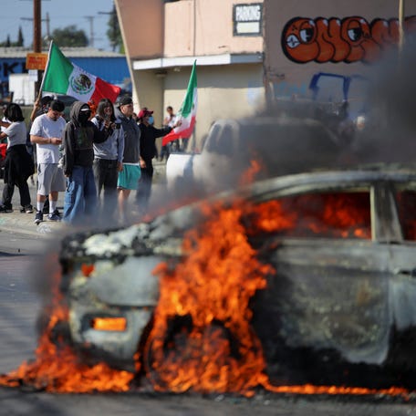 Protesters stand near a car burning in flames following multiple detentions by Immigration and Customs Enforcement (ICE), in the Los Angeles County city of Paramount, California, on June 7, 2025.