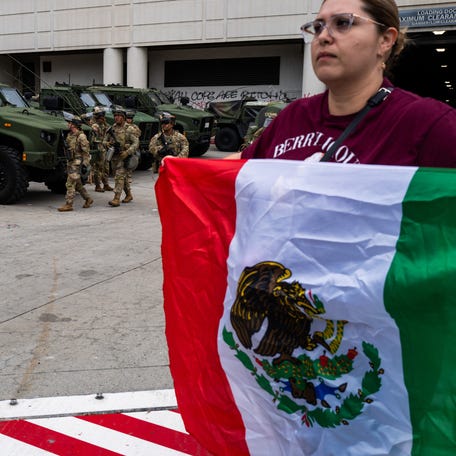 A woman walks with a Mexican flag in front of National Guard troops outside the Metropolitan Detention Center, MDC on June 08, 2025 in Los Angeles, California. Tensions in the city remain high after the Trump administration called in the National Guard against the wishes of city leaders following two days of clashes with police during a series of immigration raids. More protests are scheduled for today.
