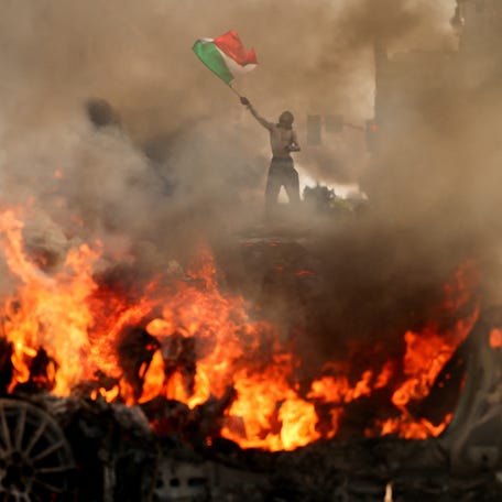 A man waves a Mexican flag as smoke and flames rise from a burning vehicle during a protest against federal immigration sweeps, near Los Angeles City Hall, in downtown Los Angeles, California on June 8, 2025.