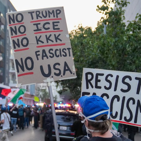 A protester holds a sign in front of law enforcement officers during a June 9, 2025, protest in downtown Los Angeles following a series of immigration raids around the metro area.