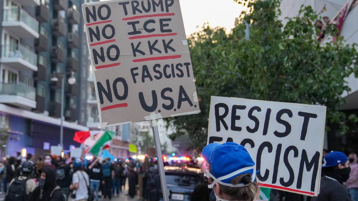 A protester holds a sign in front of law enforcement officers during a June 9, 2025, protest in downtown Los Angeles following a series of immigration raids around the metro area.