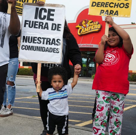 A child is assisted while holding a placard that reads "ICE, out of our communities" during a protest against federal immigration sweeps in Atlanta on June 10, 2025.