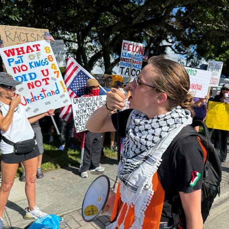 A person uses a megaphone as protesters hold signs as they take part in a "No Kings" protest against U.S. President Donald Trump's presidency and immigration policies, near Mar-a-Lago, in West Palm Beach, Florida, U.S., June 14, 2025.