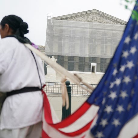A person stands with a U.S. flag attached to them, after the U.S. Supreme Court dealt a blow to the power of federal judges by restricting their ability to grant broad legal relief in cases as the justices acted in a legal fight over President Donald Trump's bid to limit birthright citizenship, outside the court in Washington, D.C., June 27, 2025.
