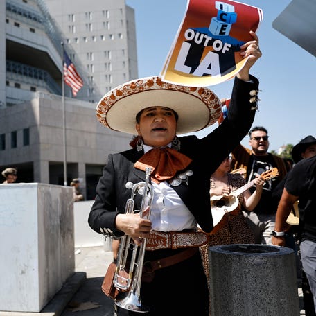 Mariachi musician Maricela Martinez holds a poster which says 'ICE out of LA' as she marches past U.S. Marines standing guard near the Metropolitan Detention Center (in background) during a protest by mariachi and folklorico dancers in response to immigration raids on June 20, 2025 in Los Angeles, California. ICE detainees are sometimes held at the detention center. A series of federal immigration raids have sparked widespread protests and compelled the Trump administration to activate members of   the California National Guard and bring in U.S. Marines against the wishes of Gov. Gavin Newsom and city leaders.