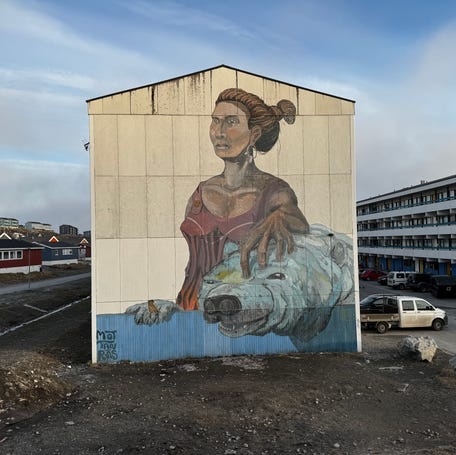 An outdoor wall mural is seen in Nuuk, Greenland, featuring an Inuit woman petting a polar bear.