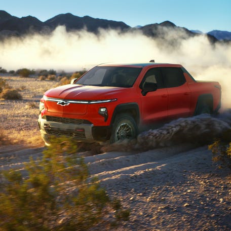 Front 3/4 view of the 2026 Silverado EV Trail Boss in Habanero Orange driving off-road.