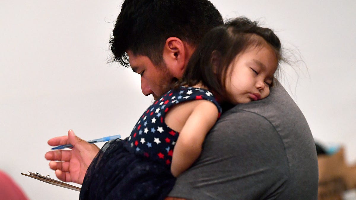 Luis Maldonado balances a clipboard in one hand as his 1-year-old daughter Gabriella sleeps on his shoulder in San Angelo Saturday July 5, 2025. His family had come to PaulAnn Church to register for assistance after floodwaters had forced them from their home the morning before.
