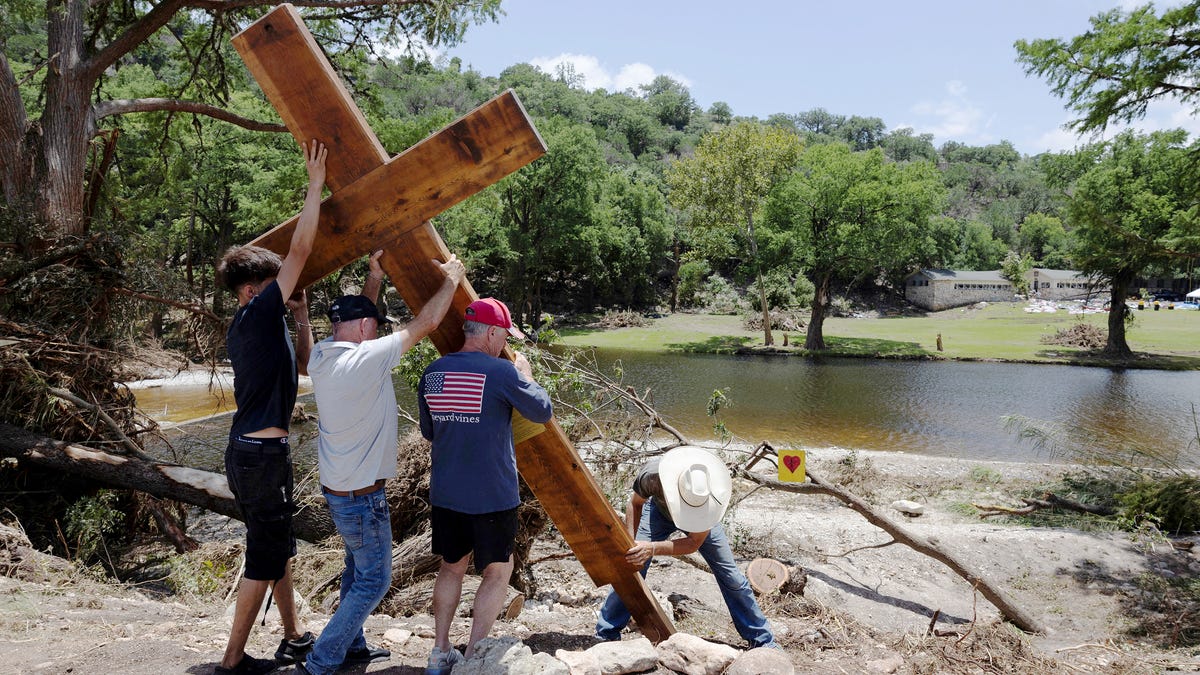 People place a cross by the Guadalupe River, across from Camp Mystic, following deadly flooding, in Hunt, Texas on July 10, 2025.