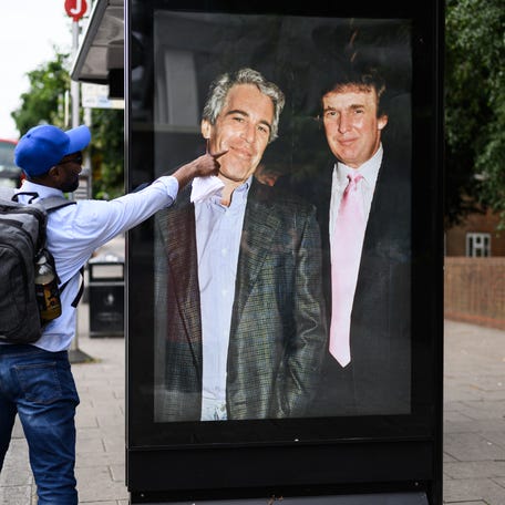 A man gestures to a photograph of US President Donald Trump and convicted child sex offender Jeffrey Epstein after it is unofficially installed in a bus shelter on July 17, 2025 in London, England. The satirical artist behind the stunt has previously targeted Elon Musk and Tesla.