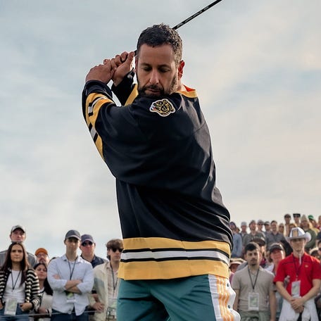 Happy Gilmore, played by Adam Sandler, breaks out his signature golf swing as caddy Oscar, played by Bad Bunny, looks on in "Happy Gilmore 2," released to stream on Netflix early July 25, 2025.