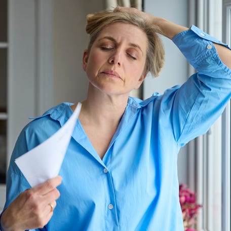 Menopausal Mature Woman Having Hot Flush At Home Cooling Herself With Letters Or Documents