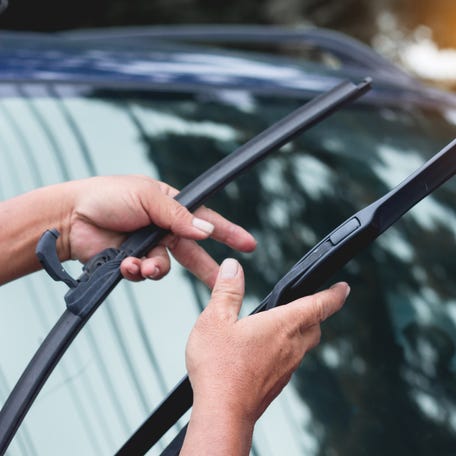 A mechanic replaces windshield wipers on a car.