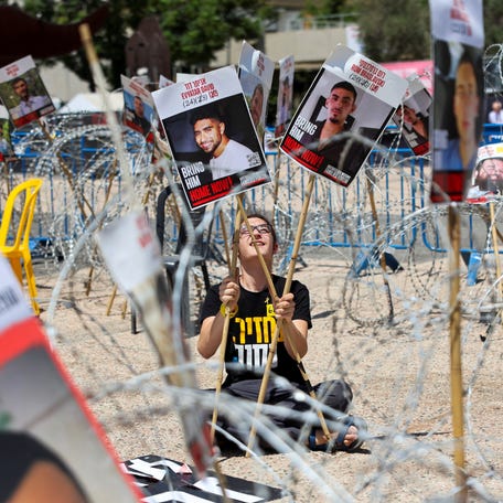 A woman holds placards with pictures of Israeli hostages Evyatar David and Rom Braslavski, held as hostages in Gaza, as she sits amid security wire, during a protest in Gaza, in Tel Aviv, Israel, August 2, 2025.