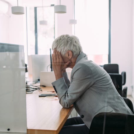 A frustrated person places their head in their hands while sitting at a desk in the office in this photo illustration.