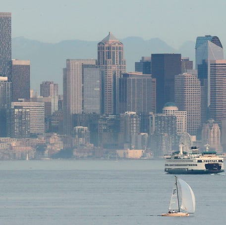 Haze hangs over the Seattle skyline as the Washington State Ferry Wenatchee and a sailboat navigate the waters, as viewed from Bainbridge Island's Rockaway Beach Road on Wednesday, Sept. 30, 2020.