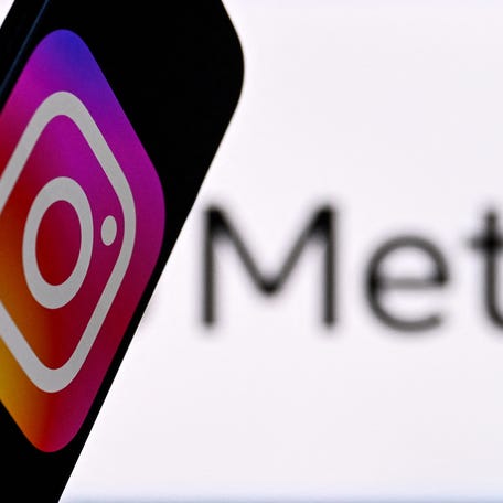 Instagram logo displayed on a smartphone in front of the media giant Meta's logo on a laptop screen.