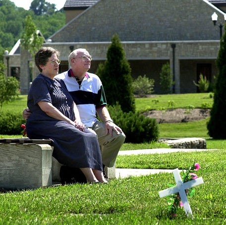 Text: 2000.0606.10.1--FUNERALS10--nikon digital image--Rita and John Wessel of Bridgetown sit on a bench near what will be their burial plot in a section of Spring Grove Cemetery Tuesday. They looked at the Jon Deitloff Funeral Centre, background, and decided to buy funeral plans for the future, thus lifting the burden of funeral planing and expense for their children. Photo by Craig Ruttle/Cincinnati Enquirer    Youâ€™ve planned out everything â€