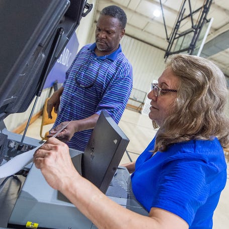 Poll workers Tina Hamby, right, and Michael Taylor, center, deal with a jammed ballot in a voting machine at Griffith Memorial Baptist Church in Jackson, Miss., during the municipal general election Tuesday, June 3, 2023.
