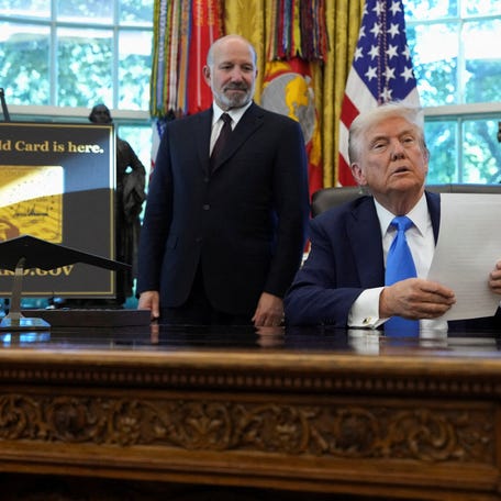 President Donald Trump looks on as he sits next to a sign that reads "Trump Gold Card is here", with Secretary of Commerce Howard Lutnick standing by his side, in the Oval Office at the White House in Washington, D.C., on Sept. 19, 2025.