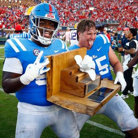 Mississippi offensive linemen Cooper Johnson (52) and Patrick Kutas (75) react with the Magnolia Bowl trophy after defeating LSU at Vaught-Hemingway Stadium.