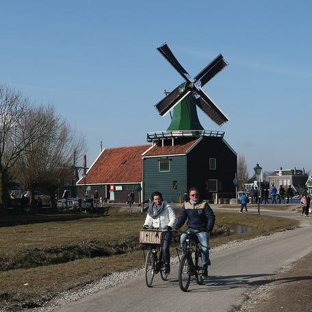 ZAANDIJK, NETHERLANDS - APRIL 01: Visitors ride past traditional houses and a windmill at the Zaanse Schans outdoor mueseum on April 1, 2013 in Zaandijk, Netherlands.