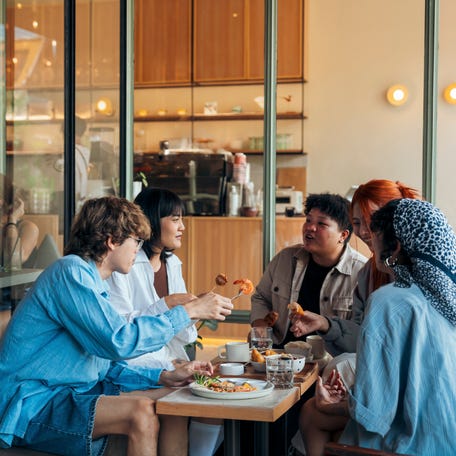 Group of diverse friends laughing and sharing breakfast at a cafe, creating a warm and lively atmosphere.