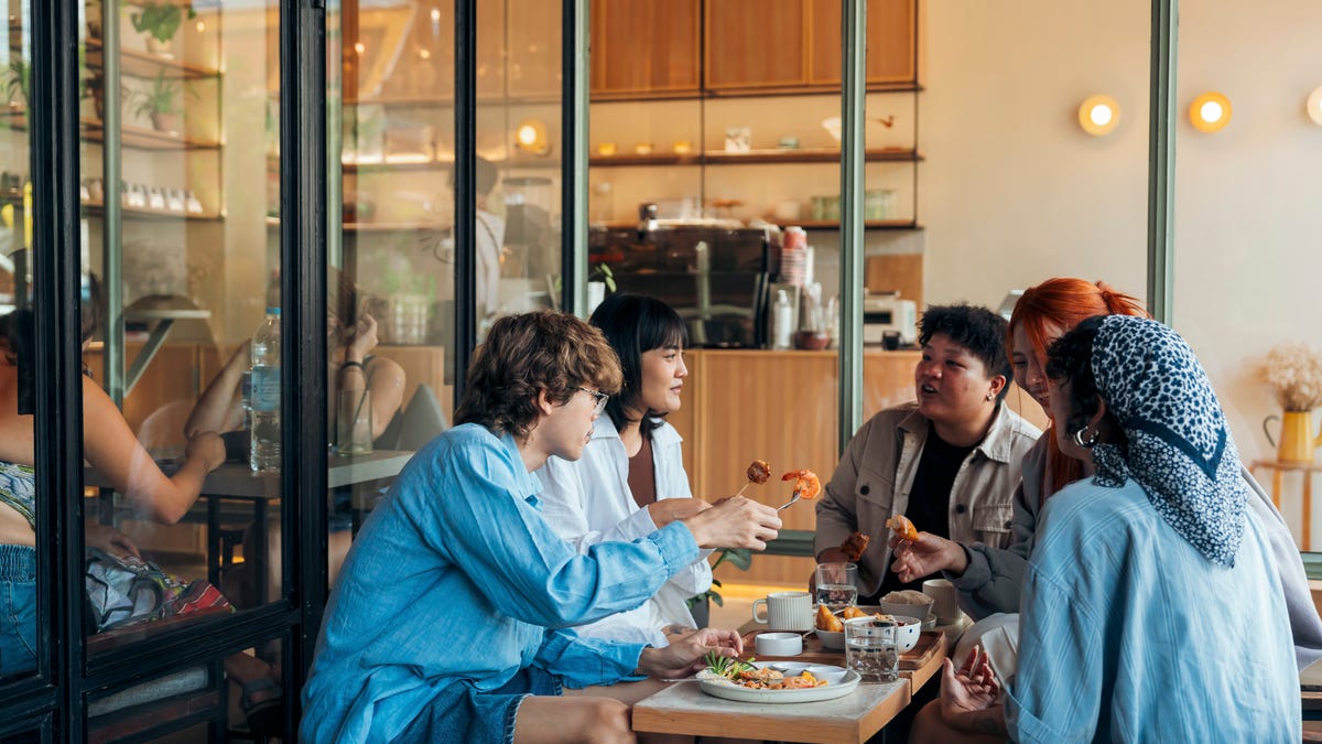 Group of diverse friends laughing and sharing breakfast at a cafe, creating a warm and lively atmosphere.