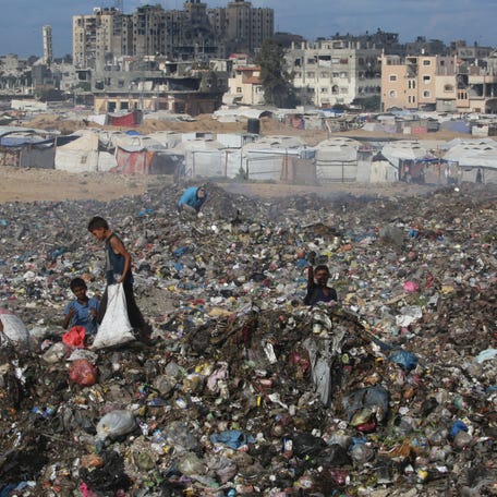 Displaced Palestinian children search of items that could be used as fuel for cooking amid a pile of garbage next to destroyed buildings at the Bureij camp for refugees in the central Gaza Strip on October 6, 2025.