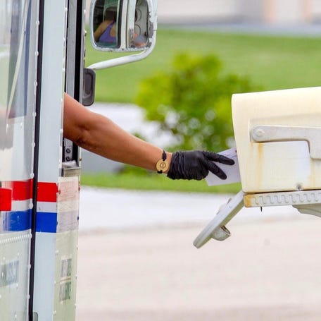 A letter carrier with the U.S. Postal Service places a letter into a mailbox while out making deliveries on a residential street on the Treasure Coast on Aug. 5, 2023.