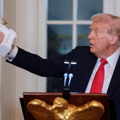President Donald Trump holds a model of an arch monument during a ballroom dinner in the East Room at the White House in Washington, D.C., U.S., October 15, 2025.