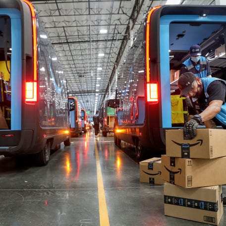 Workers load packages into Amazon Rivian electric trucks at an Amazon facility in Poway, California, on Nov. 16, 2022.