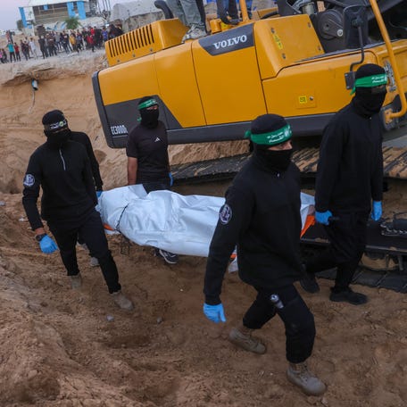 People look on as Hamas militants carry a body retrieved from a tunnel in an area north of Khan Yunis in the southern Gaza Strip on October 28, 2025. Israel's military on October 28 accused Hamas of staging its search for the remains of a Gaza hostage body, one of 28 the group had agreed to hand over under a ceasefire deal. Hamas says it is committed to the ceasefire terms, but lacks the equipment needed to locate and excavate hostage bodies potentially buried under buildings collapsed by air   strikes.