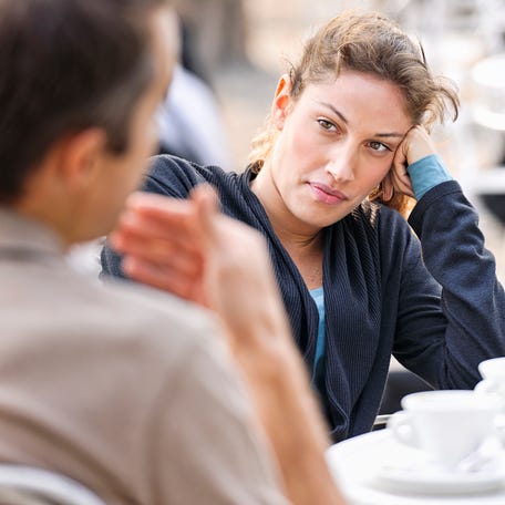 A woman listening to a man (defocussed) talking during a discussion at an outdoor cafe.