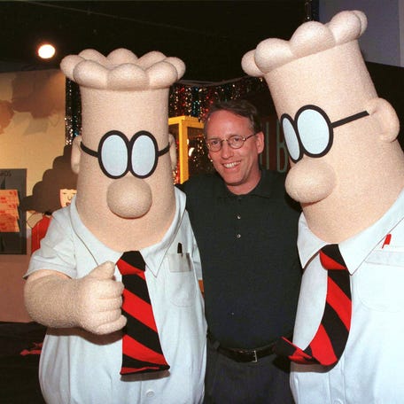 Scott Adams, the creator of "Dilbert", the cartoon character that lampoons the absurdities of corporate life, poses with two "Dilbert" characters at a party January 8, 1999 in Pasadena. The party celebrated the new half-hour animated series "Dilbert", which debuts on the UPN television network January 25.