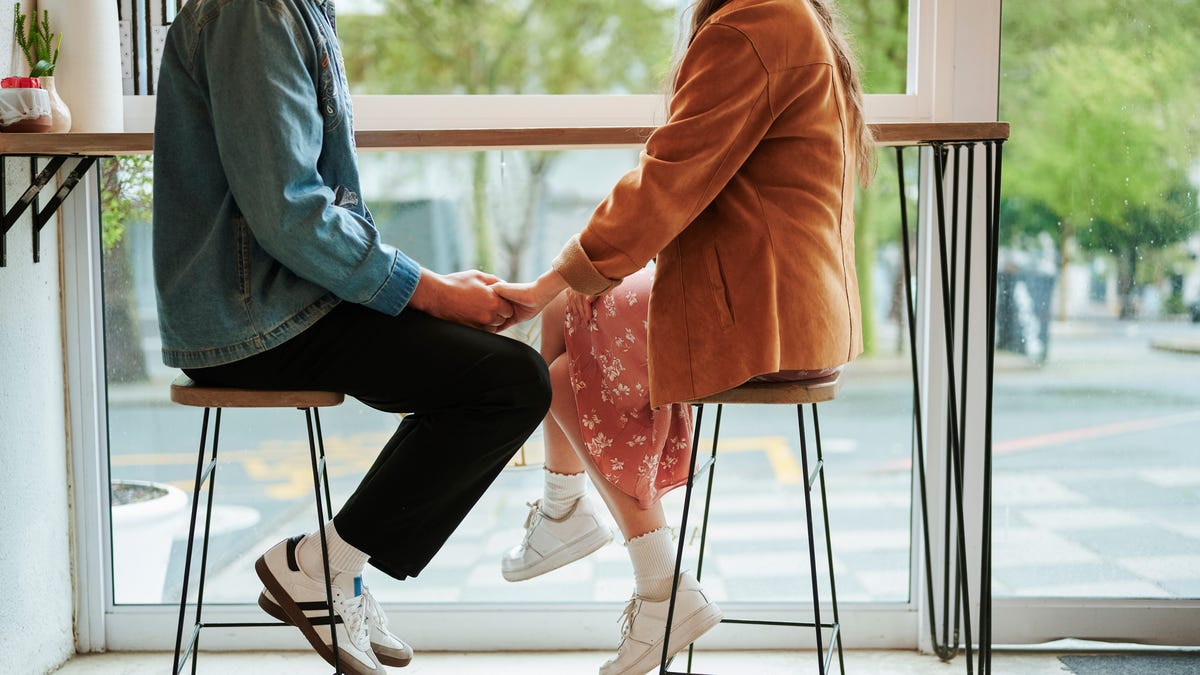 Couple holding hands while sitting together by a window in a cafe during a date