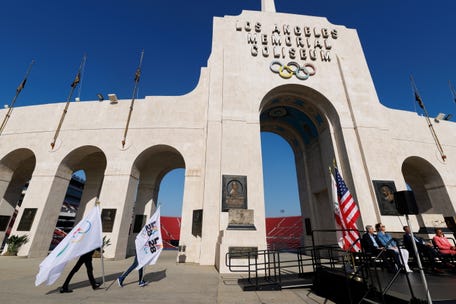LA28 workers carry Olympic flags on the day of a ceremony to announce the locations for the opening and closing of the Olympic and Paralympic games, in Los Angeles, California, U.S., May 8, 2025.