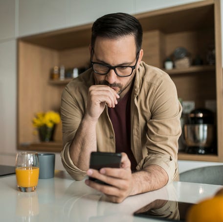 Serious man looking at his mobile phone and contemplating at home.