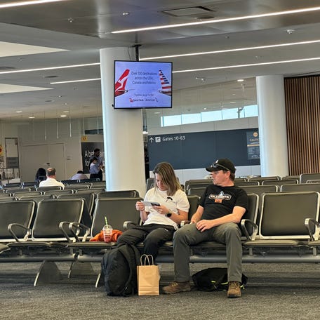 Passengers at the airport in Sydney sit below an ad for the partnership between America Airlines and Qantas.