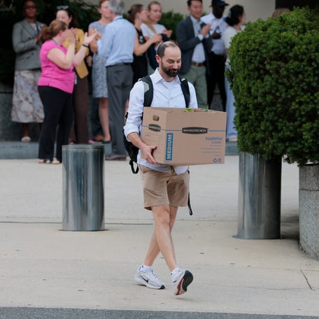 Recently laid off U.S. State Department employees carry boxes as they walk out of the Harry S. Truman Federal Building on July 11, 2025 in Washington, DC.