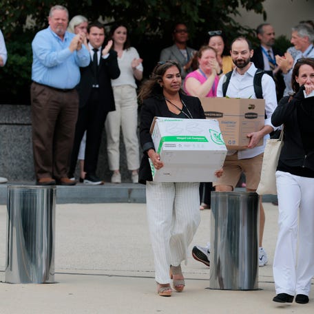 Recently laid off U.S. State Department employees carry boxes as they walk out of the Harry S. Truman Federal Building on July 11, 2025 in Washington, DC.