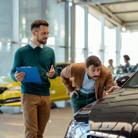 Car Salesman Showing a Car to His Customer in a Dealership Office