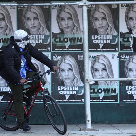 A cyclist passes posters of U.S. Attorney General Pam Bondi labelled as 