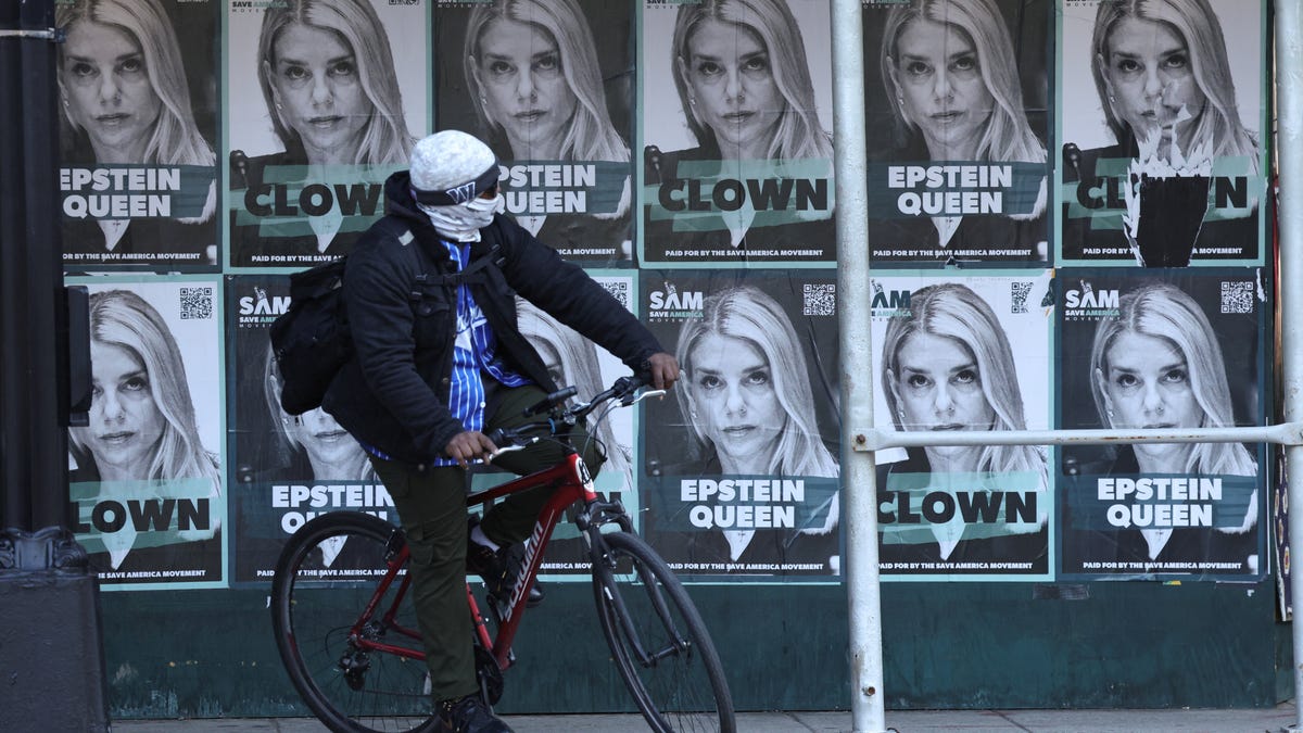 A cyclist passes posters of U.S. Attorney General Pam Bondi labelled as 