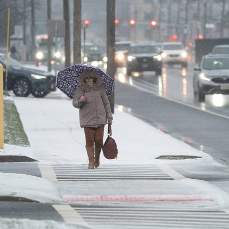 A woman walks through the snow with an umbrella in Elmwood Park, New Jersey, on Tuesday, Dec. 23, 2025.